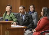 Omar Syed sits at the testifiers' table and speaks into the microphone to someone out of view. Representative Her, Maychy Vu, and Be Vang sit around him and watch him speak.